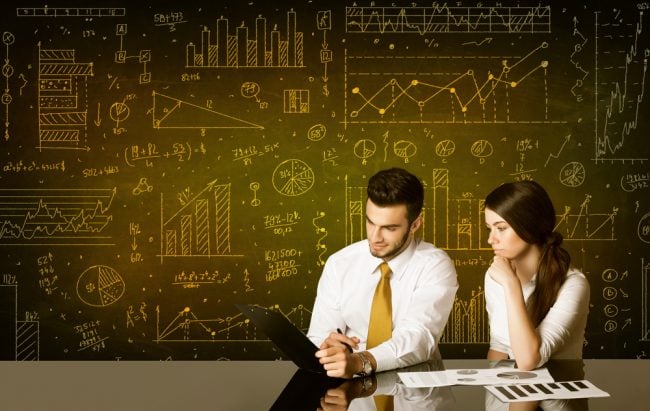 businessman and woman analyzing data at table in front of chalkboard