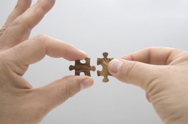 Two hands putting small puzzle pieces together.
