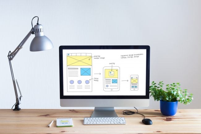 Responsive web design development technology concept with desktop computer in modern bright office and website wireframe sketch layout on screen, nobody