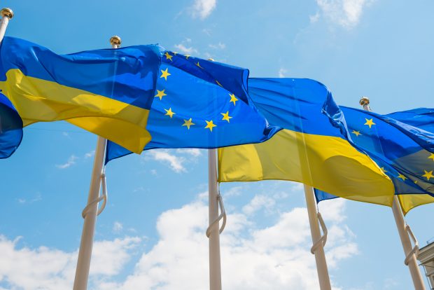 Row of flag poles with European Union and Ukraine flags fluttering by wind on blue sky background