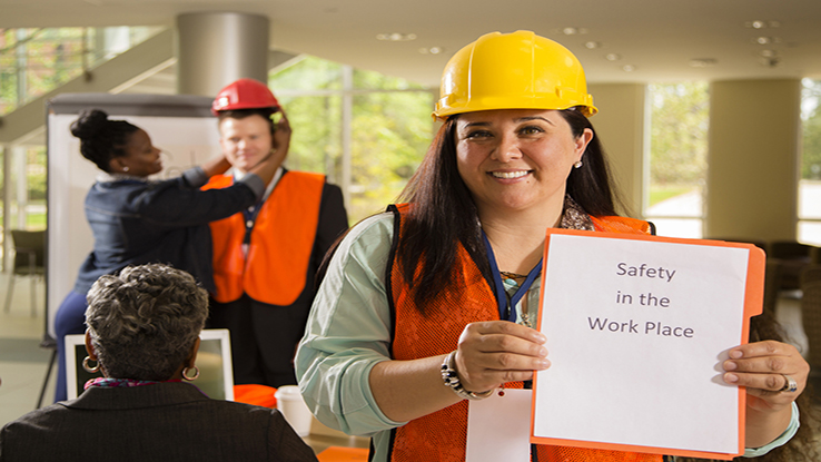 Woman in hard hat holding sign safety training with coworkers