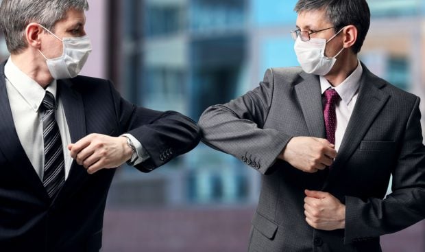 Two men wearing masks bumping elbows instead of shaking hands.