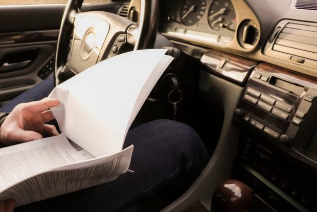A man sits in a car and holds in his hands the documents for the purchased car.