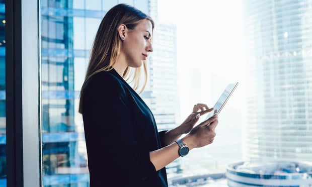 Confident professional female lawyer using app on touchpad connected to wireless internet making research in office,blonde business woman in formal wear browse via digital tablet near panoramic window. Credit: BullRun/Adobe Stock