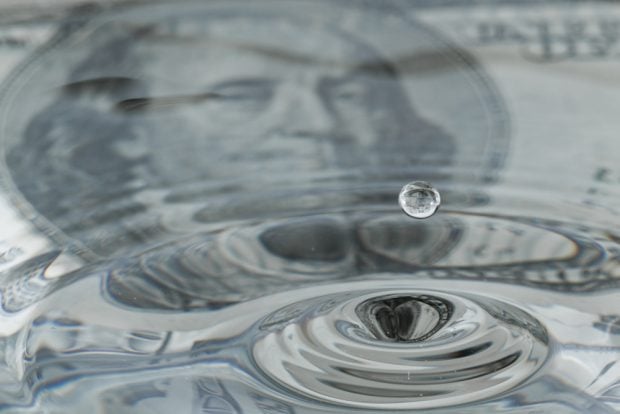 A drip of water causing a ripple effect over a dollar bill