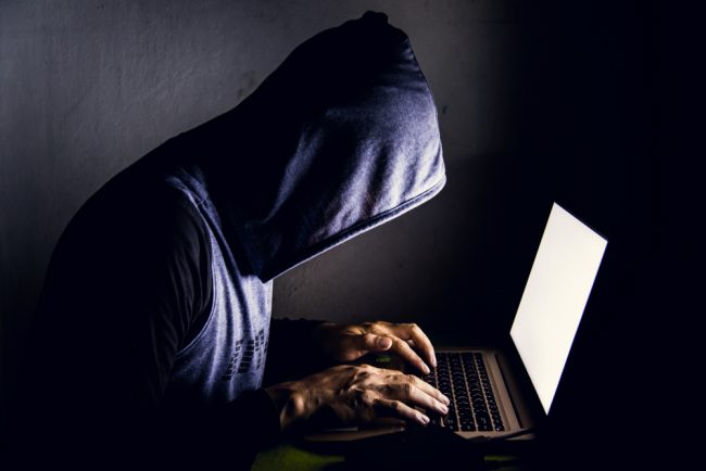 hacker in a hoodie leaning over laptop