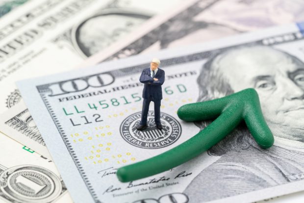man standing on $100 bills with a green arrow pointing up