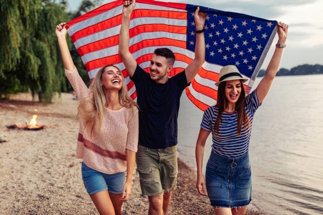three young people on beach holding American flag