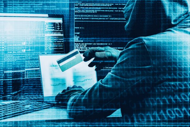 hacker seated with code on screens, laptop and payment card