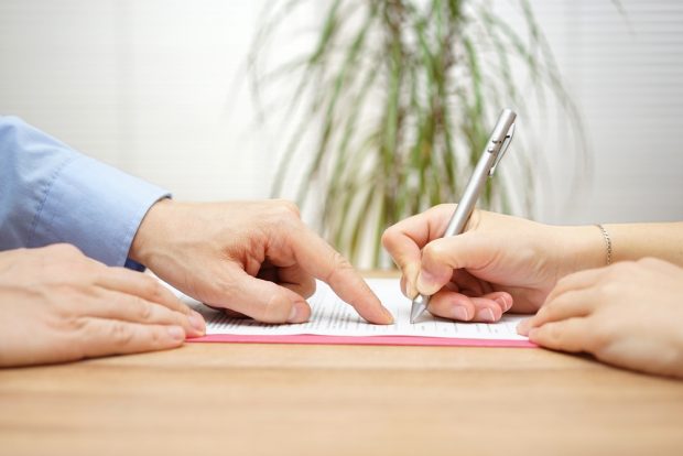 Person signing their name on a legal document as another person points where to sign.