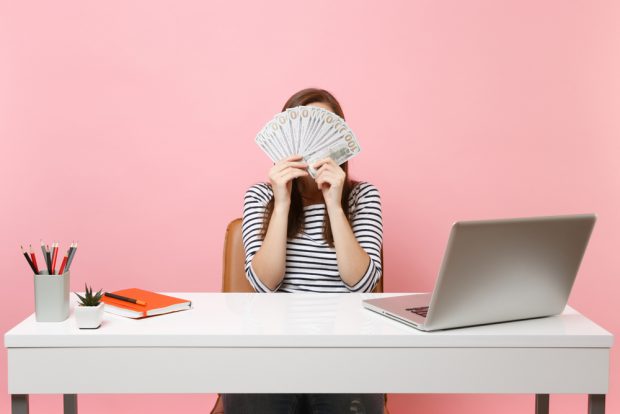 woman with cash covering her face sitting at a desk.