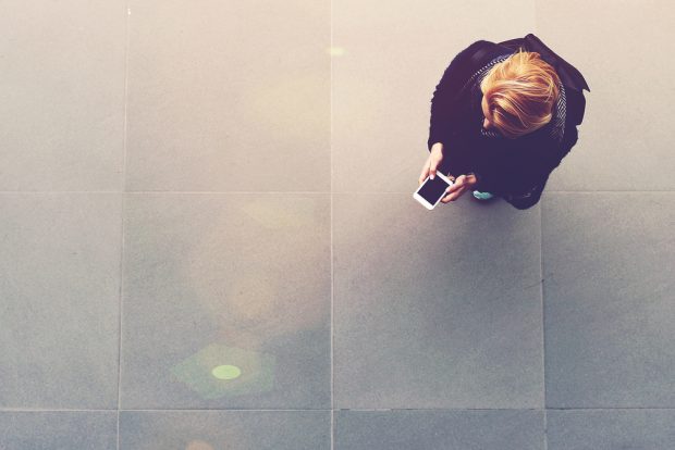 Woman stands alone in a large space while conducting mobile banking on her phone.