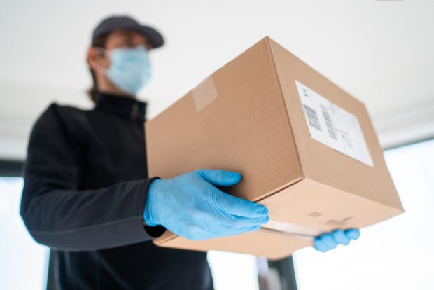 packaged being delivered to door by man wearing gloves and a mask