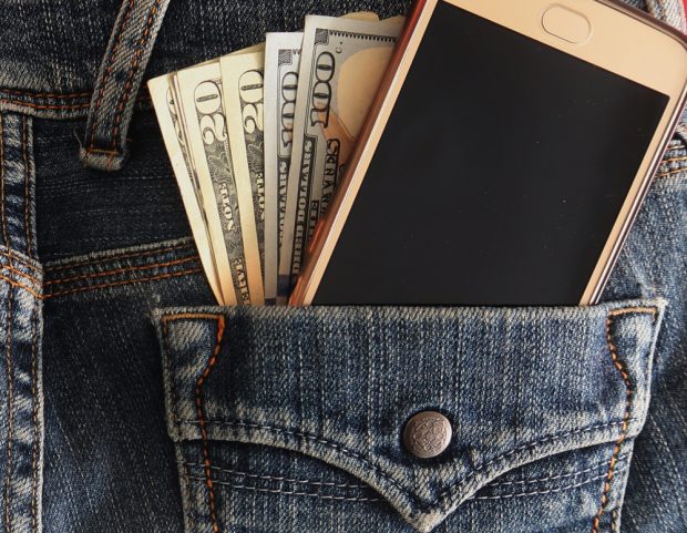 Cash and smartphone sticking out of a jean jacket pocket