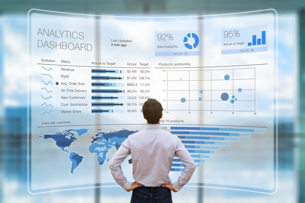 man standing in front of a large data analytics board showing graphs and patterns.