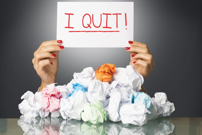woman holding up 'I quit!' sign at table with crumpled up paper