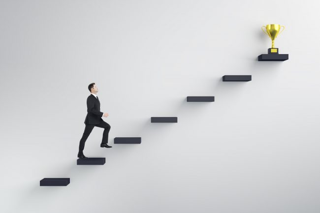 Side view of young businessman climbing stairs to success on concrete wall background