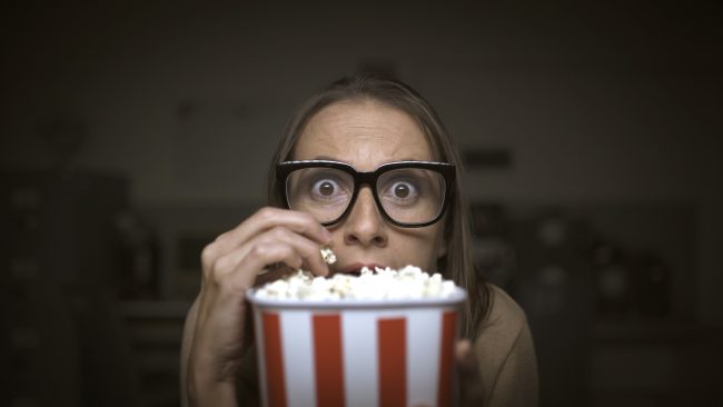 Funny scared woman watching horror movies and eating popcorn at home