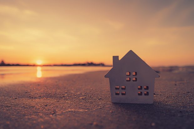 Small home model on sunset beach sand texture background. Copy space of family lifestyle and business real estate concept. Vintage tone filter effect color style.