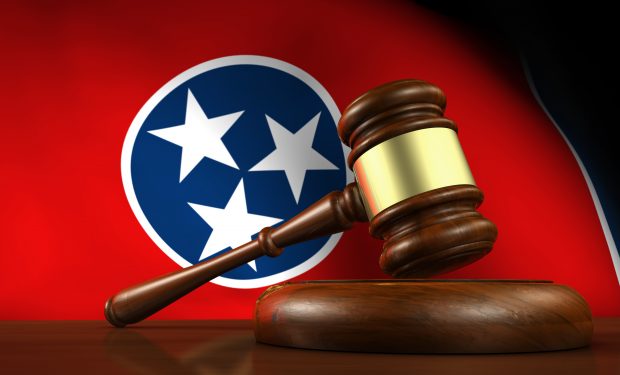 Tennessee state law, legal system and justice concept with a 3d render of a gavel on a wooden desktop and the Tennessean flag on background.