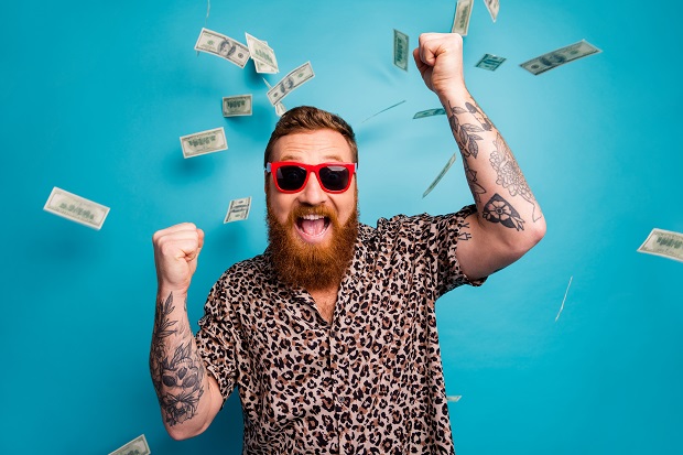 Photo of crazy handsome guy luxury rich person dollars fall from sky lottery, cashback open mouth win big money raise fists wear leopard shirt sun specs isolated blue background