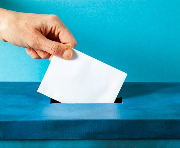 Hand putting ballot in blue election box