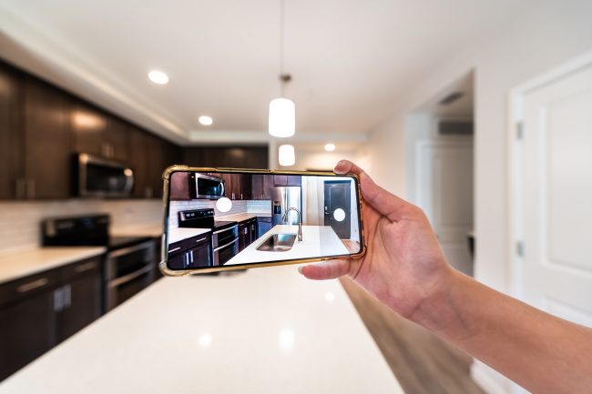 Hand photographing house apartment kitchen island room for sale or rent with phone smartphone closeup point of view in modern luxury condo home with blurry bokeh background