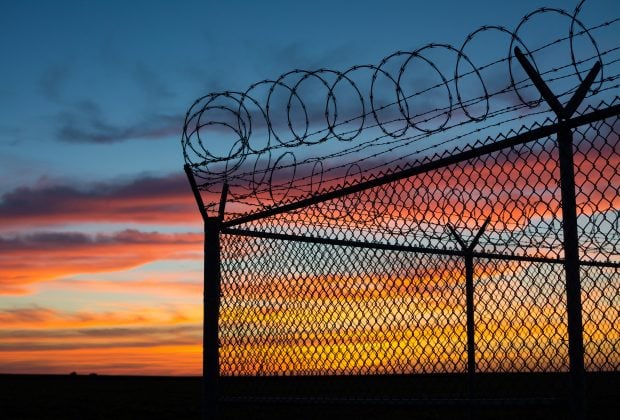 Dramatic sunset with chain link fence and razor wire silhouette.