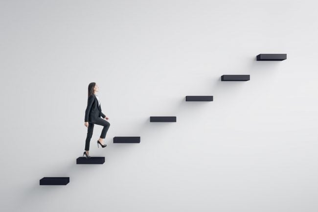 Side view of young businesswoman climbing stairs to success on concrete wall background