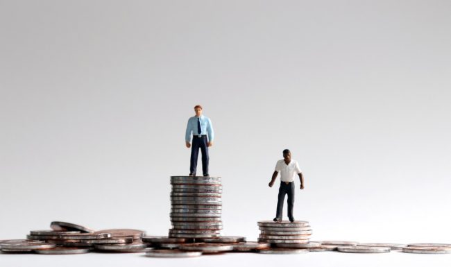 Black man standing on shorter pile of cash than white man